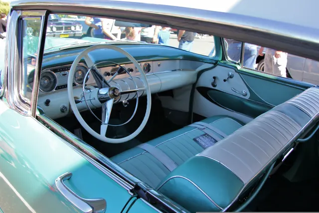 Exact-year hardtop sedan cabin showing the dashboard, steering wheel, instruments, controls, front bench, and door trim; upholstery and restoration details remain car-specific.