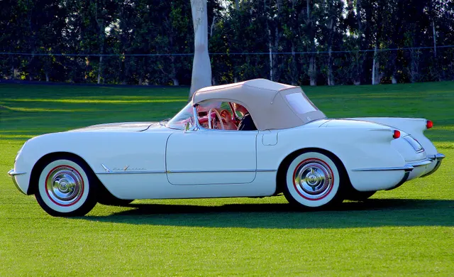 Side and rear view of a Polo White 1955 Corvette showing the two-seat proportions, raised soft top, rear-fender shape, and chrome bumper treatment.