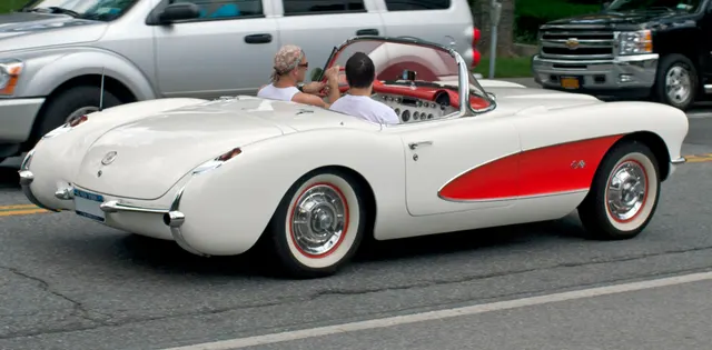 Rear and cockpit view of a Polo White and red-cove 1956 Corvette showing the rear trim, open cabin, wheel covers, and cove transition.