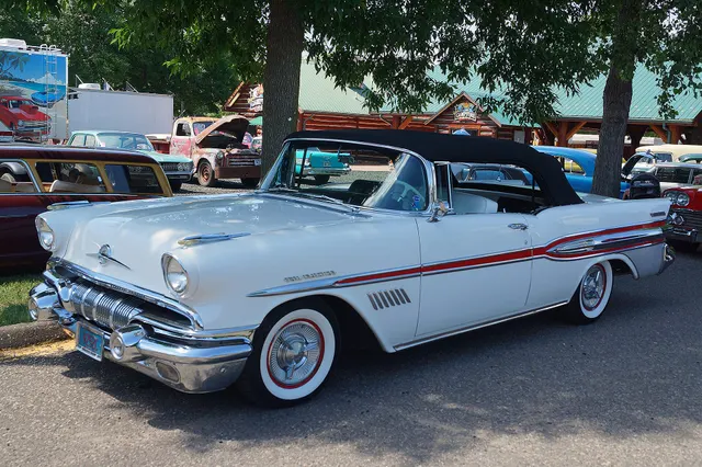 Exact-year side view showing the restored white finish, red side spear, brightwork, wheel covers, whitewalls, and black convertible top; finish and restoration remain specific to the photographed car.