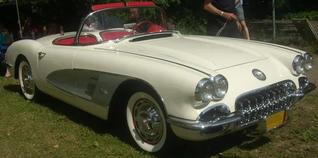 Stock-presenting Snowcrest White 1959 Corvette roadster with silver coves, red cabin, full wheel covers, and whitewalls.