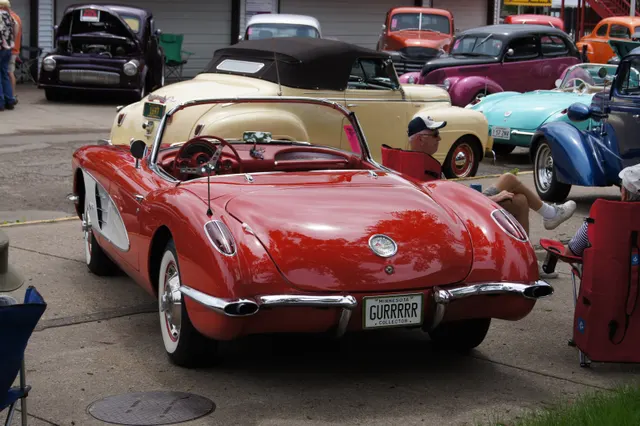Open Roman Red 1959 Corvette in rear three-quarter view with white coves and red interior.