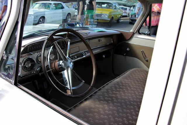 Exact-year Coronet sedan driver's area retained for the full-width seat, upholstery, door trim, steering wheel, horizontal speedometer, dashboard, column controls, and cabin proportions.