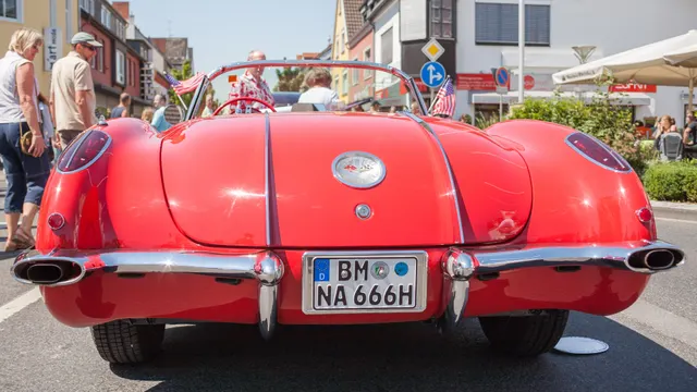 Low front view of a restored Roman Red and Ermine White 1960 Corvette, showing the quad headlamps, tooth grille, split bumpers, and cove trim.