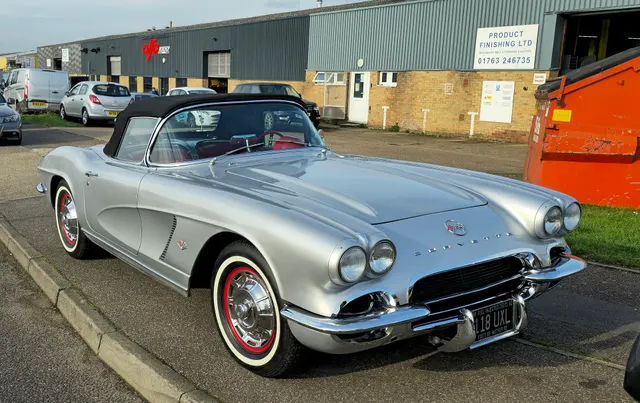 Stock-presenting Sateen Silver 1961 Corvette with white coves, red interior, auxiliary hardtop, and factory-style wheel covers.