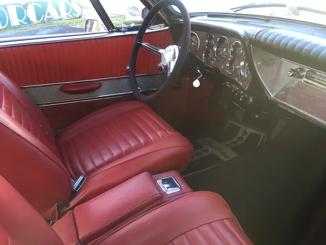 Exact-model cockpit showing the bucket seats, console, two-spoke wheel, three-plane instrument cluster, metal passenger-side dash overlay, horizontal seat pleats, and door trim.