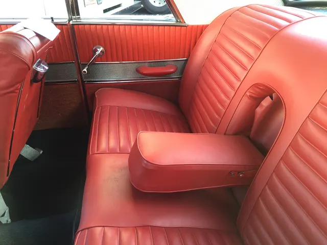 Exact-model rear cabin showing the horizontal-pleat upholstery, fold-down center armrest, vertically pleated side panels, bright trim, and carpet.