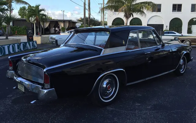Rear three-quarter view documenting the recessed rear glass, blade-like quarters, body-color tail-lamp housings, checkered deck overlay, bumper, and hardtop proportions.