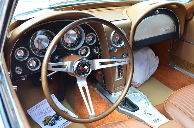 Restored 1963 split-window coupe cabin showing the twin-cowl dash, center console, Powerglide controls, and bucket seats.