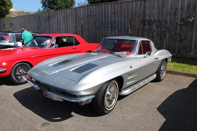 Restored silver 1963 Corvette split-window coupe showing the concealed-headlamp nose and turbine-style wheel-cover presentation.