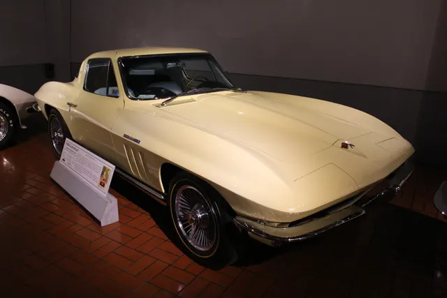 Museum-displayed 1965 coupe with standard exhaust routing, model-year fender louvers, and turbine-style wheel covers.