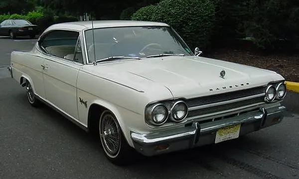 Front three-quarter view of a white exact-year Marlin showing the quad headlamps, grille, Rambler hood letters, ornament, fender script, bright trim, and factory-style wire covers.