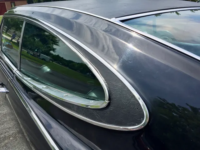 Close exact-year view of the teardrop side window, bright surround, pillarless opening, and optional black vinyl roof covering.