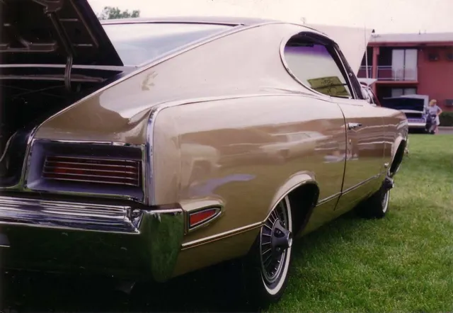 Exact-year rear three-quarter view showing the fastback roof and side glass, tunneled tail lamp, rear quarter, bright trim, wheel cover, and open trunk context.