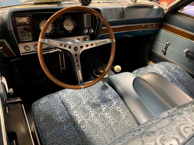 Exact-year 343 four-speed cabin showing the T-10 floor shifter, patterned bucket seats, dashboard, instruments, wood-rim steering wheel, woodgrain trim, and pedals.