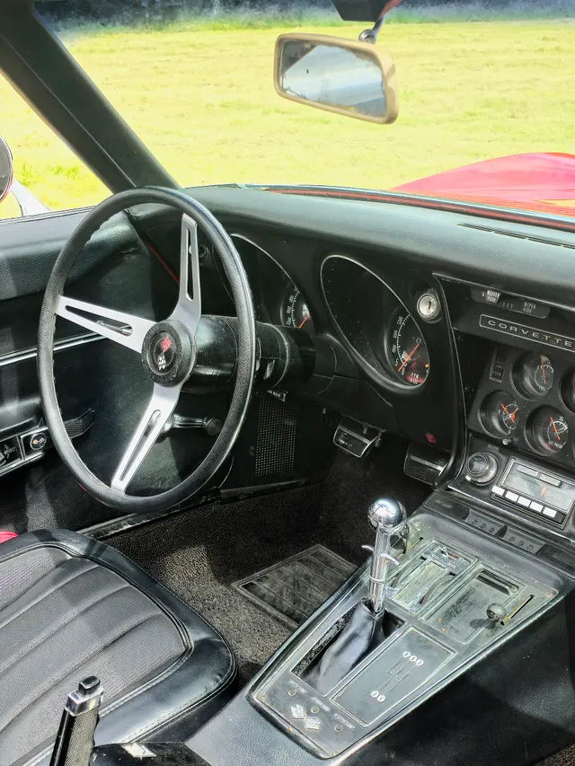 Black 1968 cabin showing the three-spoke wheel, speedometer and tachometer, center-stack gauges, full console, four-speed shifter, and parking brake.