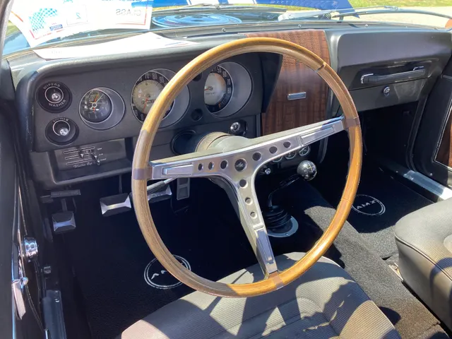 Cabin of the same restored 1969 AMC AMX 390 Go Package example, showing the two-seat layout, instrument panel, wood-rim wheel, and four-speed floor controls