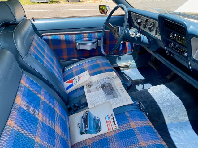 Front cabin of the same 1970 Hornet SST showing the blue plaid upholstery, reclining front seats, door trim, dashboard, steering wheel, and controls.