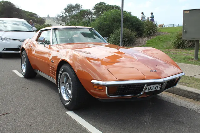 Low front three-quarter view of an orange coupe showing the concealed lamps, grille texture, chrome bumper, and fender vents.