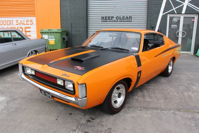 Front three-quarter view of an exact-year Hemi Orange E49 showing the black bonnet treatment, scoop, R/T and 4 graphics, grille, driving lamps, and alloy wheels.