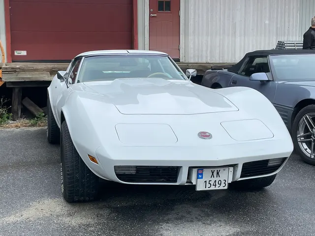 White coupe head-on view highlighting the integrated bumper cover, paired lower grilles, parking lamps, concealed headlamps, and cold-air hood.