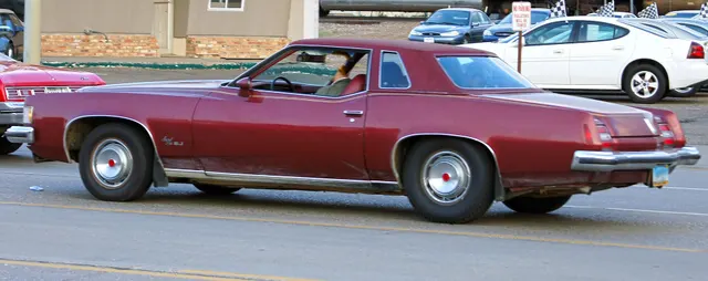 Exact-year SJ rear and side view retained for package script, pinstriping, quarter window, deck, tail lamps, below-bumper plate location, full wheel covers, and stance; the crop, wear, and one-car condition remain disclosed.