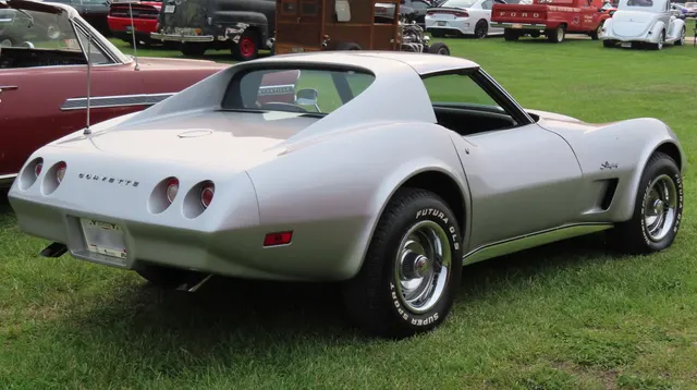 Silver 1974 coupe in rear three-quarter view, highlighting the sloping urethane rear cover, four round taillamps, fixed rear glass, and removable roof panels.