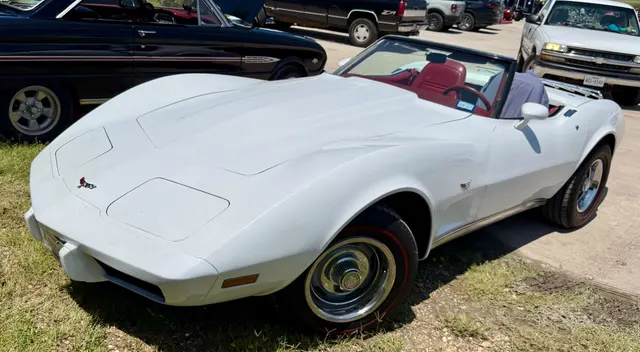 White 1974 Corvette convertible in front three-quarter view, showing the open two-seat body, urethane nose, Rally wheels, and red cabin.