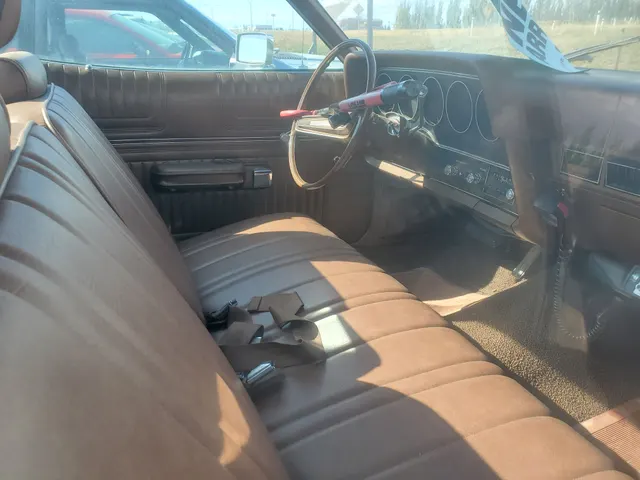The photographed 1974 Ranchero cabin showing its bench seat, dashboard, instruments, steering wheel, radio, and door trim; loose belts, papers, and the red steering-column lock are excluded from factory-equipment evidence.