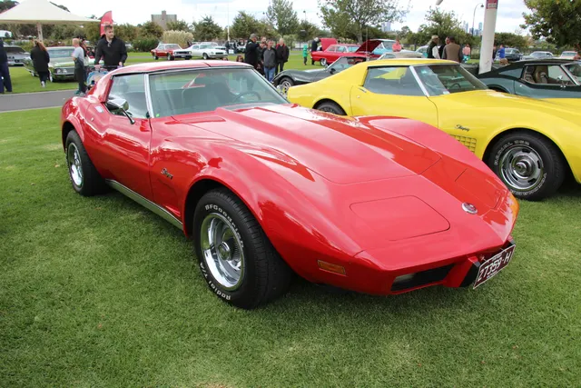 Red 1975 coupe in front three-quarter view, retained for hood, windshield, roof-panel, body, wheel, and trim context; modern tires do not authenticate original equipment.