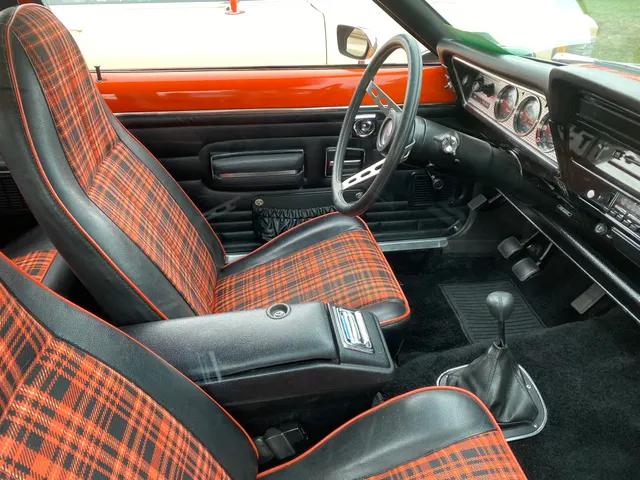 A photographed 1977 Gremlin X cabin showing plaid sport seats, black trim, dashboard, instruments, steering wheel, doors, console, and manual shifter; finish, restoration, equipment, and condition remain specific to this car.
