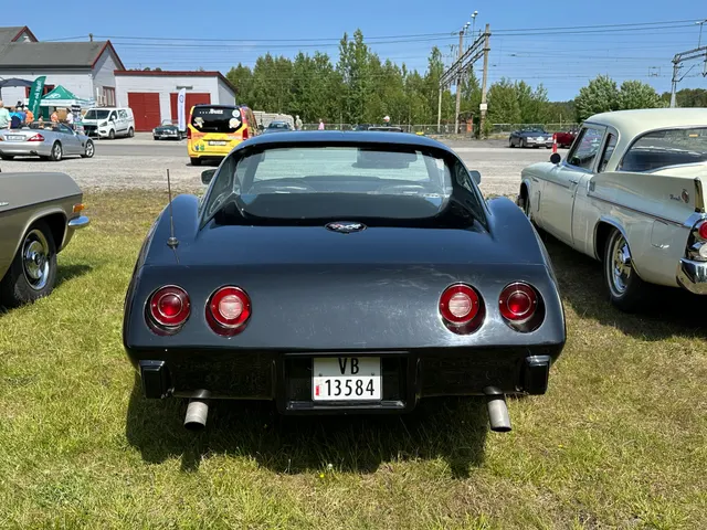 Black 1977 coupe in direct rear view, showing the fixed rear glass, filler-door emblem, four round lamps, urethane tail, license recess, and dual exhaust outlets.
