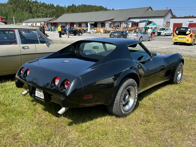 The same black 1977 coupe in rear three-quarter view, showing the roof panels, rear glass, fender curve, Rally wheels, short deck, tail lamps, and bumper-cover corners.