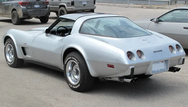 The same silver coupe in rear three-quarter view, showing fixed rear glass, removable roof panels, the short rear deck, four round lamps, urethane tail, and dual exhaust outlets.
