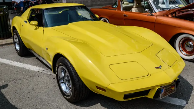 Yellow 1977 coupe in front three-quarter view with its roof panels installed, showing the hood, windshield, fender vent, concealed headlamps, urethane nose, and C3 proportions.