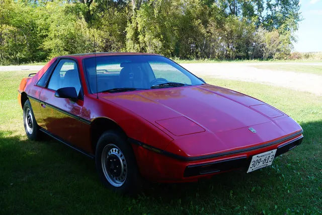 Exact-year Fiero 2M4 SE front-quarter view retained for the wedge profile, closed retractable lamps, windshield, mirrors, black body-side treatment, and steel-wheel context.